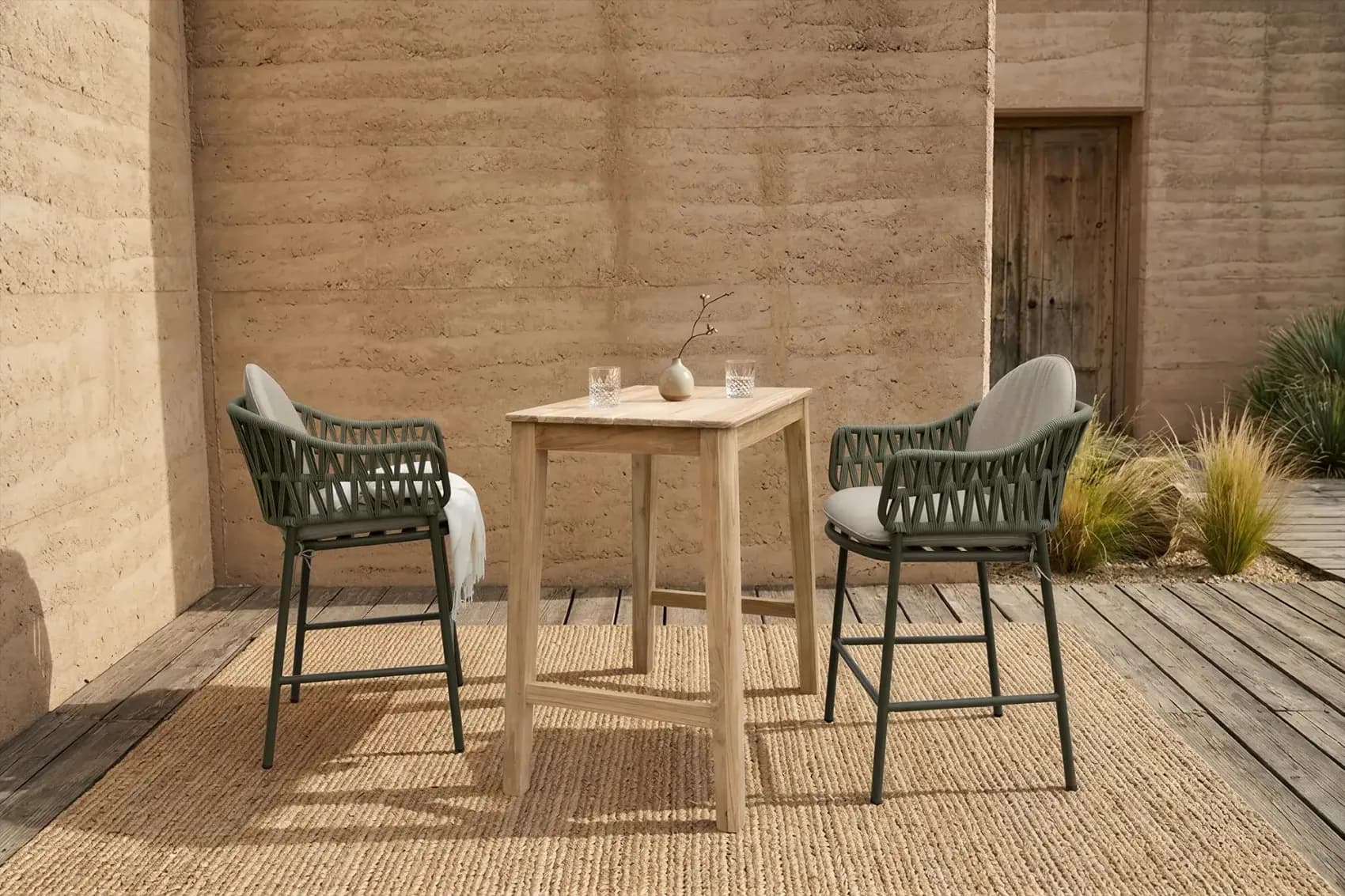 Two rope bar chairs and a high teak table on a wooden deck