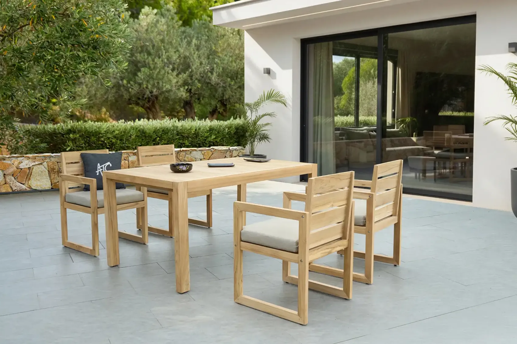 Teak dining table with four armchairs on a paved patio
