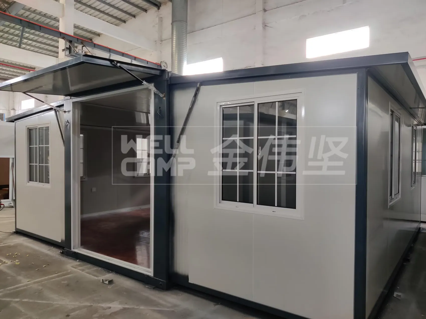 Expandable container house with open side wings in a factory hall